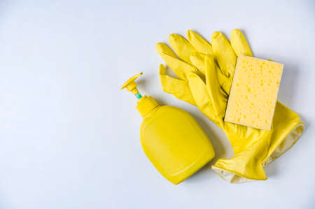Yellow gloves, sponge and detergent on a pale background. The concept of cleaning or washing dishesの写真素材