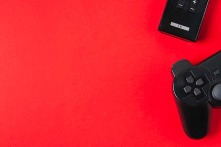 Game joystick and TV remote on bright red background