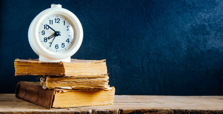 White alarm clock and old books on old wooden tableの写真素材