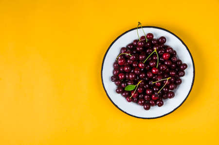 Fresh cherry berries in old white plate on yellow backgroundの写真素材