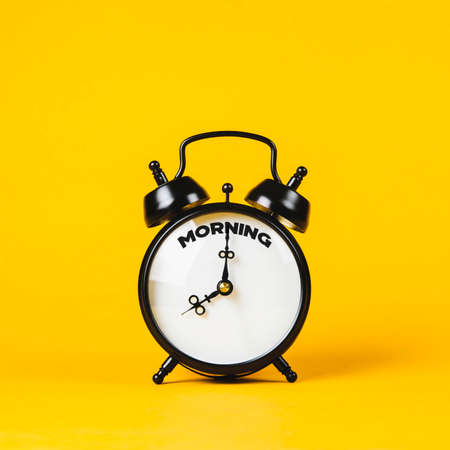 Vintage alarm clock and text Morning on it on yellow background