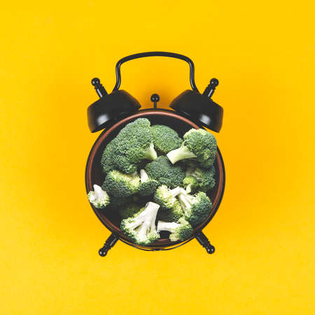 Collage of alarm clock and a plate of broccoli on a yellow backgroundの写真素材