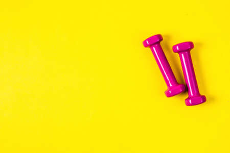 Pink dumbbells on an yellow background, a concept of sports or weight loss