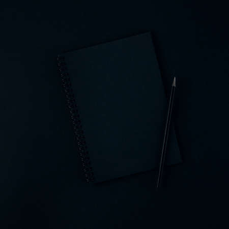 A black notebook and pencil on a dark black background