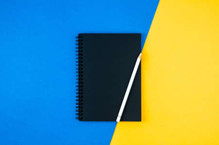 A black notebook and pencil on a blue yellow backgroundの写真素材