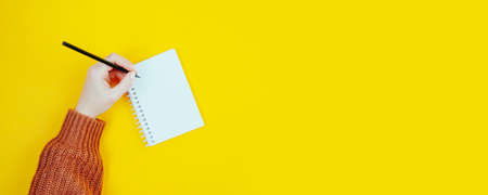 The hand of a left-handed woman holds a pencil in her hand. International concept for a left-handed person on a yellow backgroundの写真素材