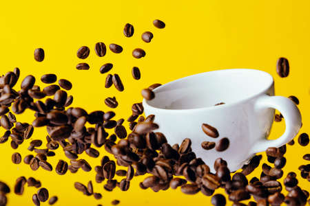 Flying coffee beans and a white Cup on a bright yellow backgroundの写真素材