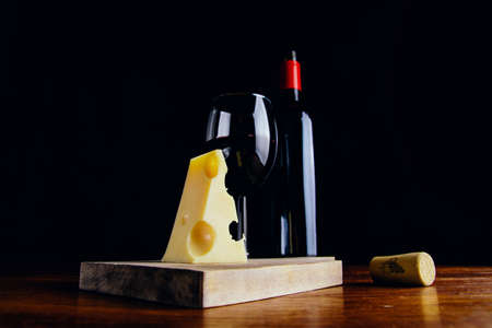 A glass of red wine, a bottle and a piece of cheese on a wooden table and a dark backgroundの写真素材