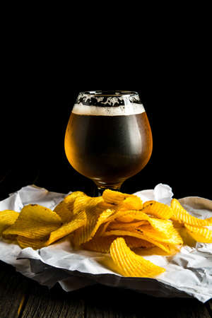A glass of beer and potato chips on a wooden table and a dark backgroundの写真素材