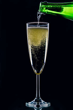 Sparkling wine pours from a bottle into a glass on a dark backgroundの写真素材