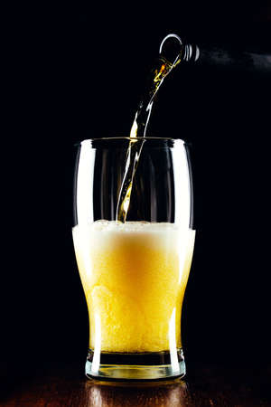 Lager beer pours from a bottle into a glass on a black backgroundの写真素材