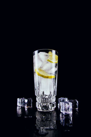 A glass of gin and tonic with lemon and ice cubes on black backgroundの写真素材