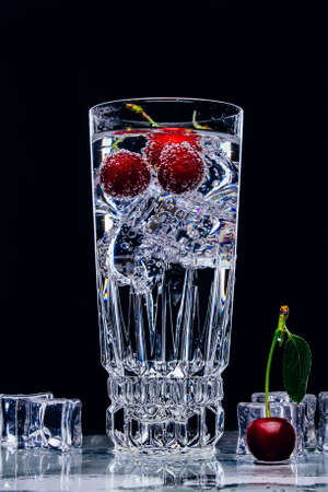 A glass of gin and tonic with cherry and ice cubes on black backgroundの写真素材