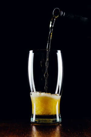 Lager beer pours from a bottle into a glass on a black backgroundの写真素材