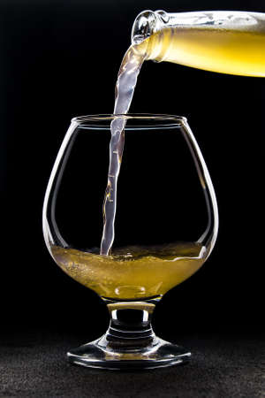 Fruits beer pours from a bottle into a glass on a dark backgroundの写真素材