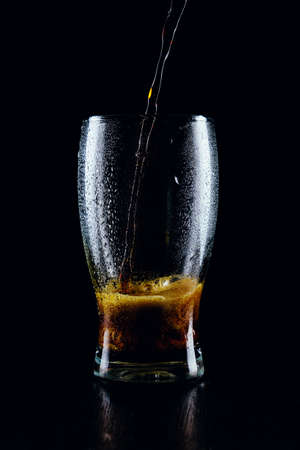 Porter beer pours from a bottle into a glass on a black backgroundの写真素材