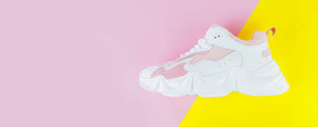 White and pink sports sneakers on a pink yellow backgroundの写真素材