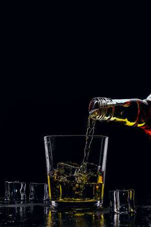 Whiskey pours from a bottle into a glass on a dark backgroundの写真素材