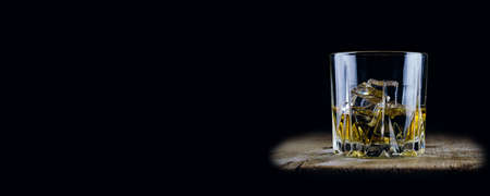 A glass of whiskey with ice cubes on a wooden table and a dark backgroundの写真素材