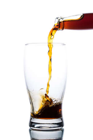 Brown ale pours from a bottle into a glass on a light backgroundの写真素材