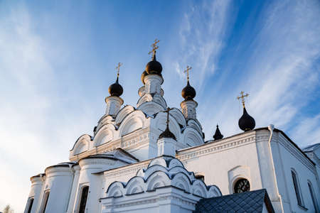 White beautiful Orthodox Church under construction in winter time. Snowy panorama of blue sky and...