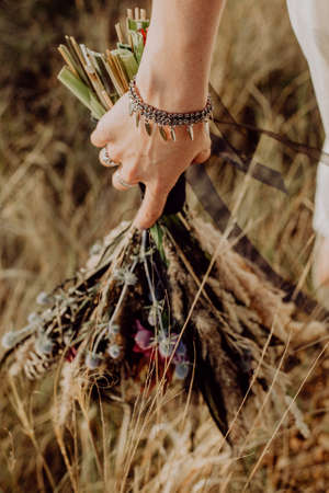 wedding bouquet in boho style collected from wild flowers, the bride holds a bouquet in her hand, in nature, white dress, live plants, a composition of dried flowersの写真素材