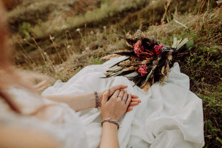 wedding bouquet in boho style collected from wild flowers, the bride holds a bouquet in her hand, in nature, white dress, live plants, a composition of dried flowersの写真素材