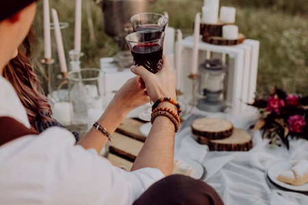 outdoor wedding, glass of red wine in hand, newlyweds sitting on the grass, festive table, boho styleの写真素材