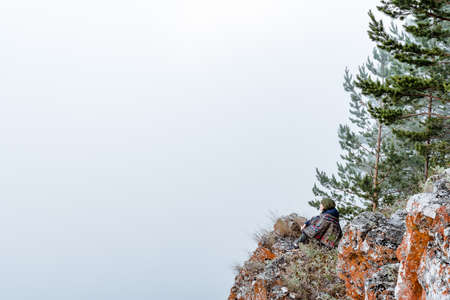 a young girl of European appearance dressed in a poncho meditates in nature, sitting in the Lotus position on the edge of a cliff in the early morning, Zenの写真素材
