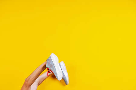 sneakers are worn on hands on a yellow background, red laces, a concept for a fashion blog or...