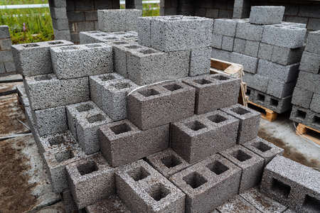 cinder blocks of gray concrete are neatly stacked in a pile, slender rows of bricks, material for...