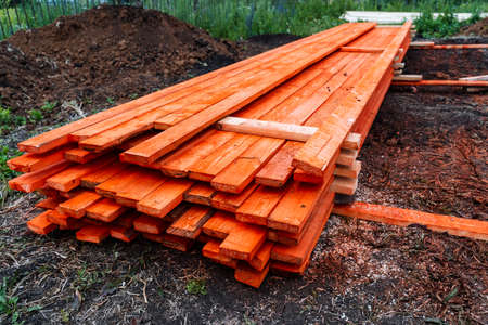 pine boards painted with red stain, lumber for construction are lying on the ground, long floor boards are stackedの写真素材