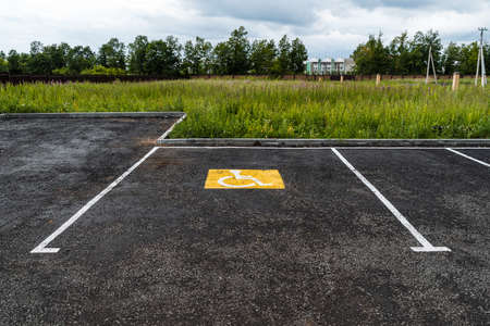 a yellow sign on the asphalt shows a Parking place for people with disabilities, a road sign, markings on the roadの写真素材