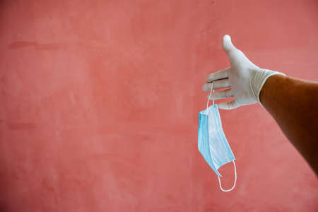 a hand in a white medical glove stretches forward, a sweaty hand under latex, fingers spread out against a maroon wall, hand protectionの写真素材