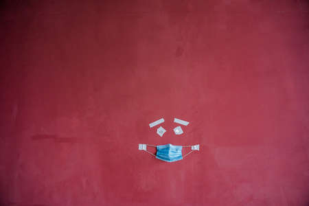 visual art of the image of a person's face on the wall, creative approach to the image of a patient in a mask, protective medical mask in a minimalistic concept, drawing on a maroon wallの写真素材