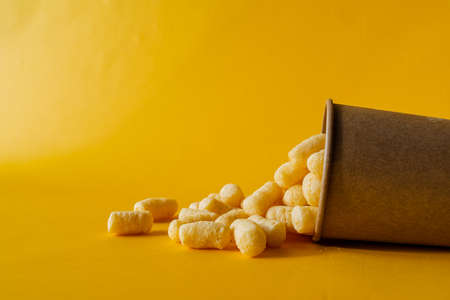 yellow corn sticks in a glass on a colored background, a full box of sweet corn sticks, a treat for children, yellow background, minimalismの写真素材