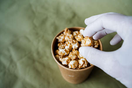 a hand takes sweet popcorn from a brown jar, a box of popcorn on a colored background, a gloved hand...