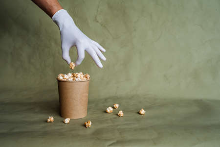 hand in a white glove reaches for popcorn, take food in protective gloves, hold a piece of food with two fingers, a full box of popcorn, security at the fast food distribution, minimal conceptの写真素材