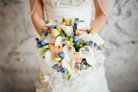 Bridal bouquet, hold the wedding bouquet in your hand, satin ribbons adorn the wedding bouquet of roses, on the background of the brides dress, fresh flowers, made by a floristの写真素材
