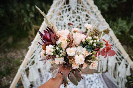 Bridal bouquet, hold the wedding bouquet in your hand, satin ribbons adorn the wedding bouquet of roses, on the background of the bride's dress, fresh flowers, made by a floristの写真素材