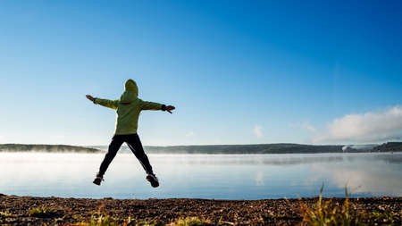 A child jumps on the lake shore. Silhouette of a jumping boy. A little boy in an autumn jacket is...