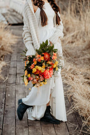 Bridal bouquet, hold the wedding bouquet in your hand, satin ribbons adorn the wedding bouquet of roses, on the background of the bride's dress, fresh flowers, made by a floristの写真素材