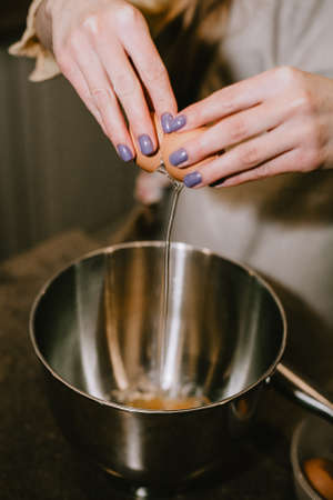 Break an egg into a saucepan. A girl breaks eggs in a bowl to make pastries. The process of baking with your own hands.の写真素材