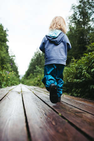 A child in a blue jacket walks along the path. A little boy climbs the mountain on his own. Children's outdoor trekking in natureの写真素材