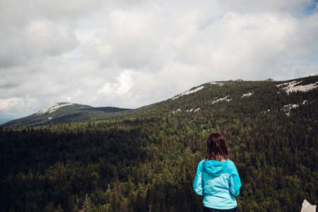 a young girl in a blue jacket stands high in the mountains and enjoys the view, enjoy the beauty of...