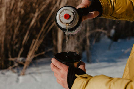 pour tea into a mug from a thermos, drink hot tea in nature, hike, eat in nature, warm up with hot coffee in winter, brew teaの写真素材