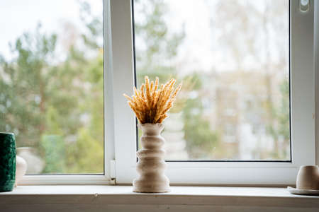 A vase of abstract shape stands in the middle of a light window sill in the workshop. Bouquet of yellow dried flowers in a vase. High quality photoの写真素材