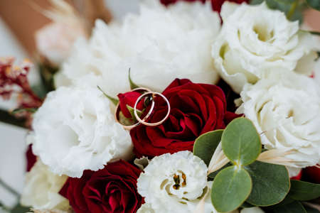 Gold wedding rings lie neatly among the red and white flowers from the wedding bouquet. High quality photoの写真素材