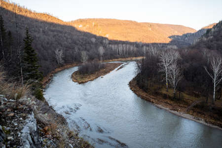 View of the river between the mountains, the river has two channels. Ahead of the mountain, part of the peaks is illuminated by the bright sun, the other part of the peaks is in the shade. High quality photoの写真素材