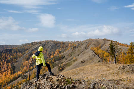 A guy in bright sportswear walks along the top of the mountain, looks forward at the mountains and forest, clear sky overhead, autumn landscape. High quality photoの写真素材